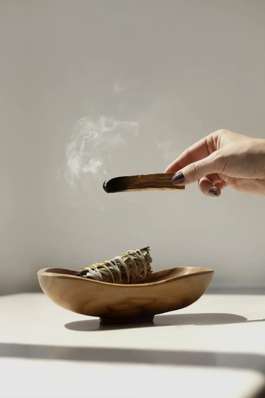 Hand holding smoking palo santo above a wooden bowl