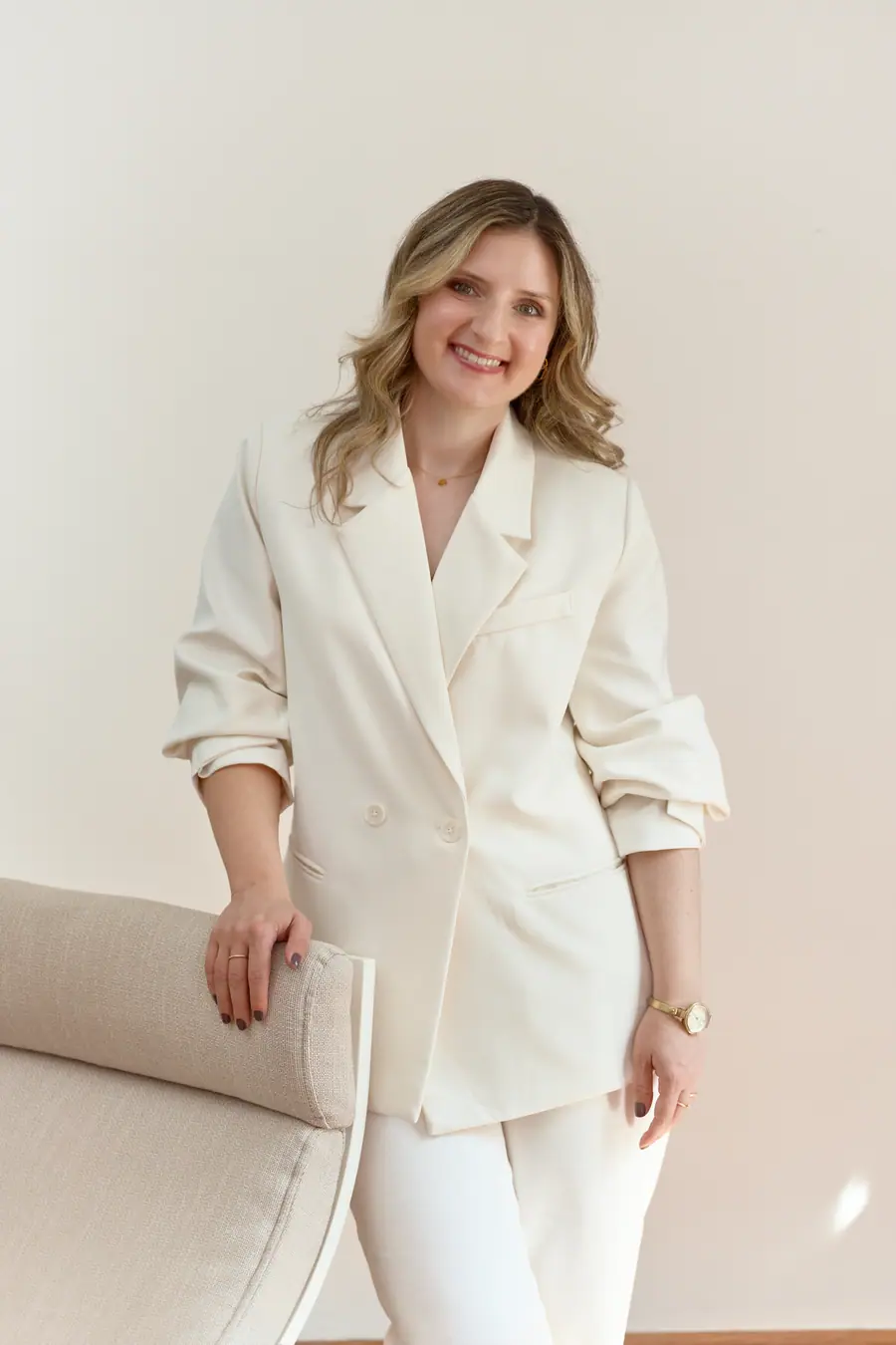 Woman in a cream suit standing beside an armchair