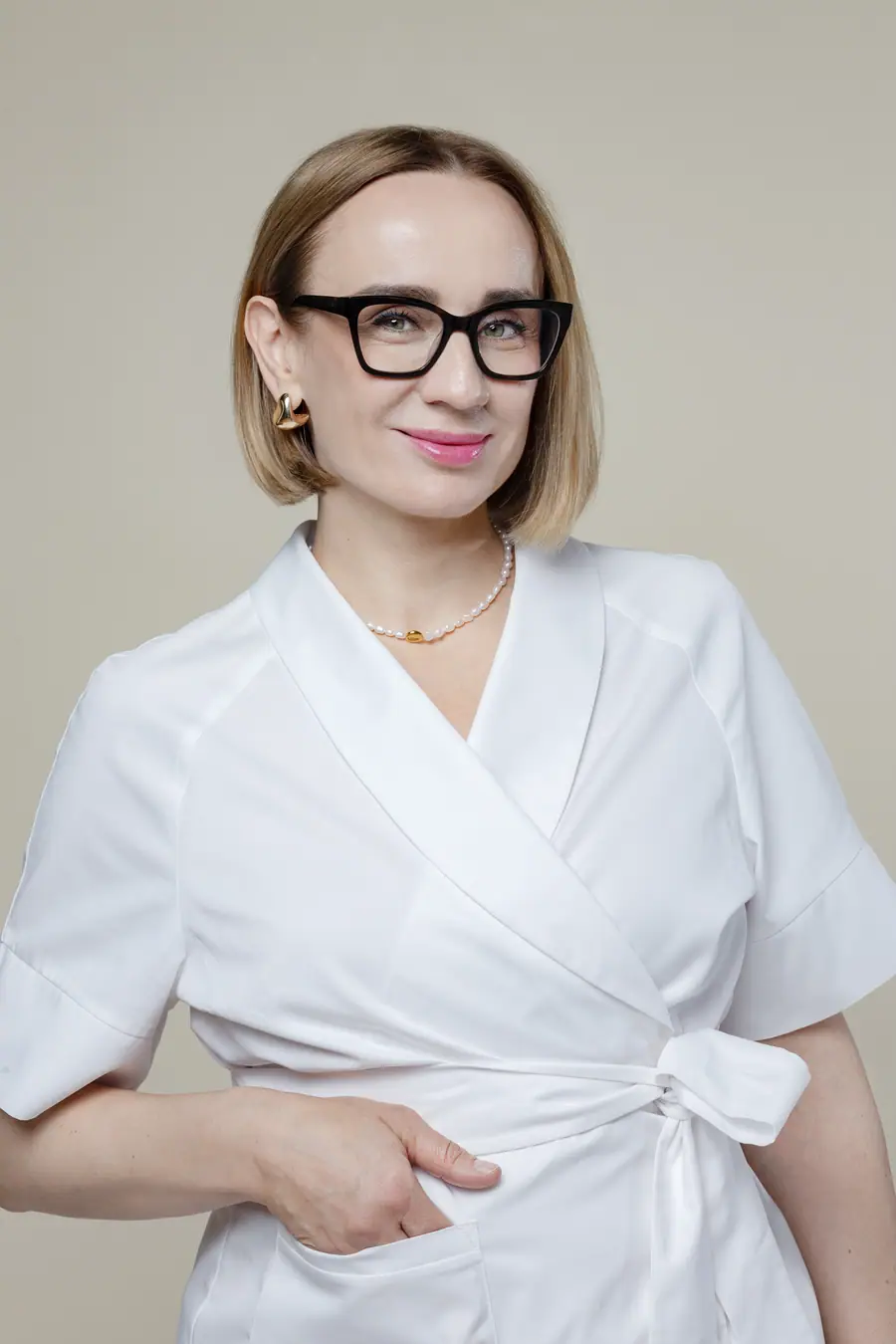 Woman in a white uniform and glasses against a beige wall
