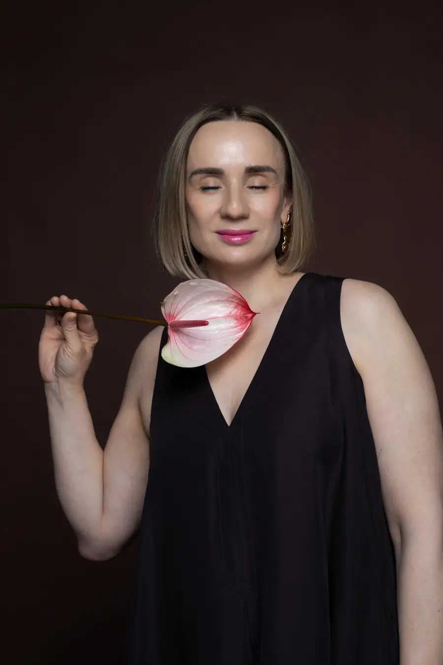 Woman in a black dress holding a flower to her cheek, eyes closed