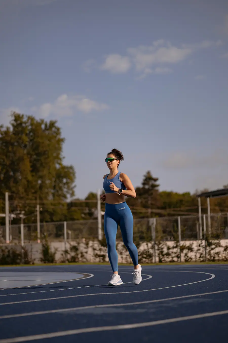 Woman running on a track, wide frame under open sky