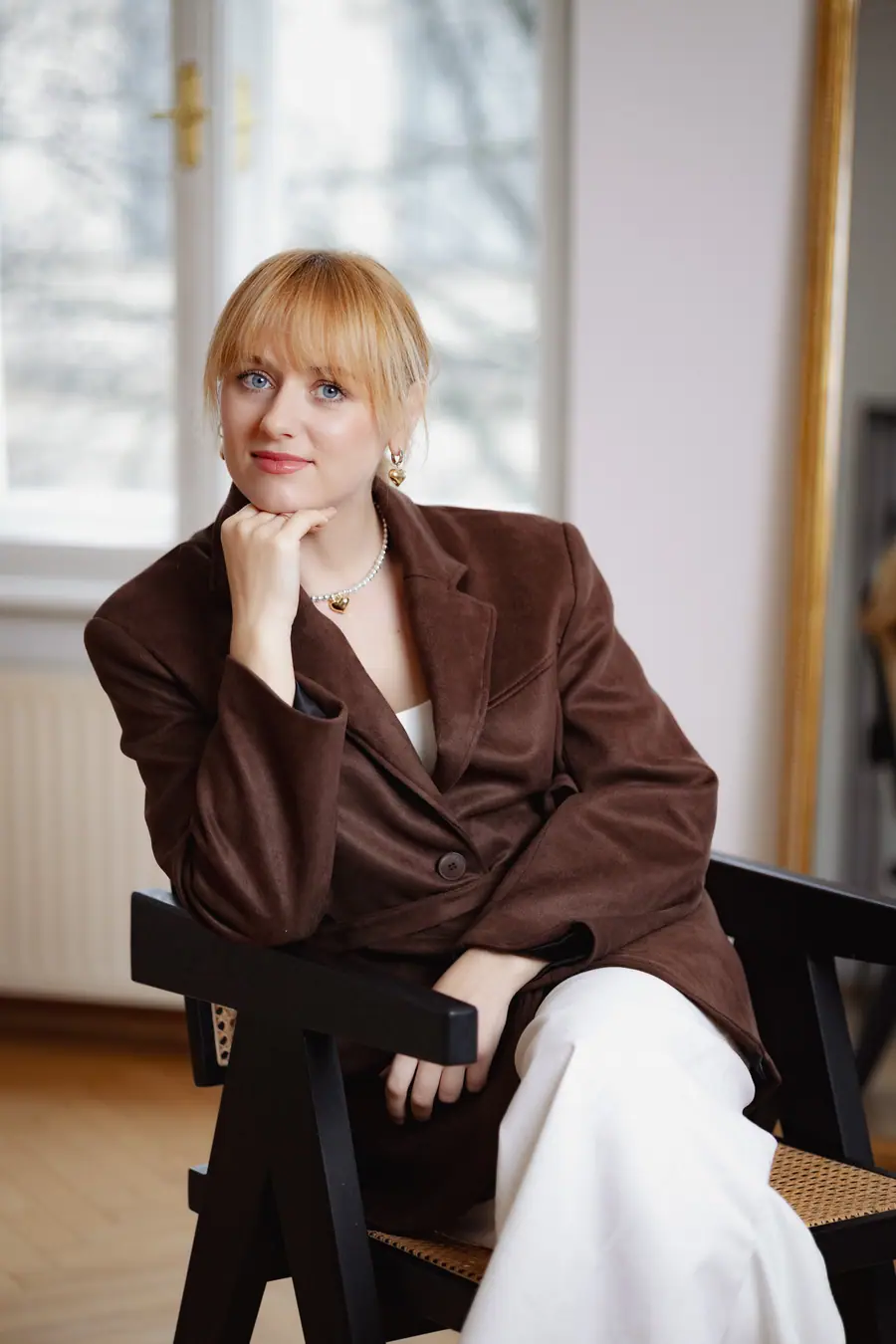 Woman in a brown blazer seated, hand to chin