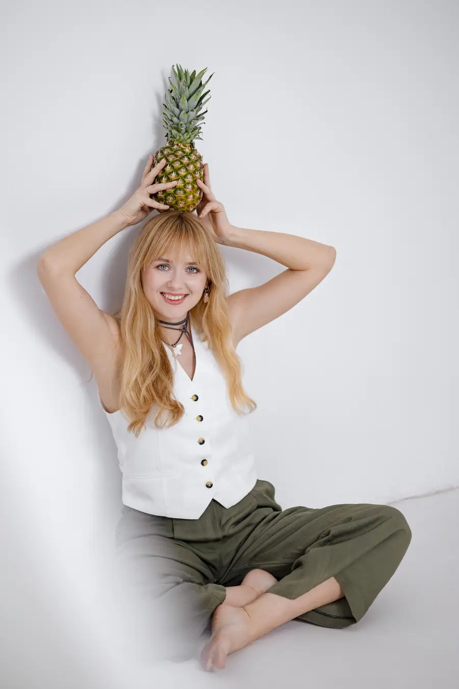 Woman seated on the floor balancing a pineapple on her head