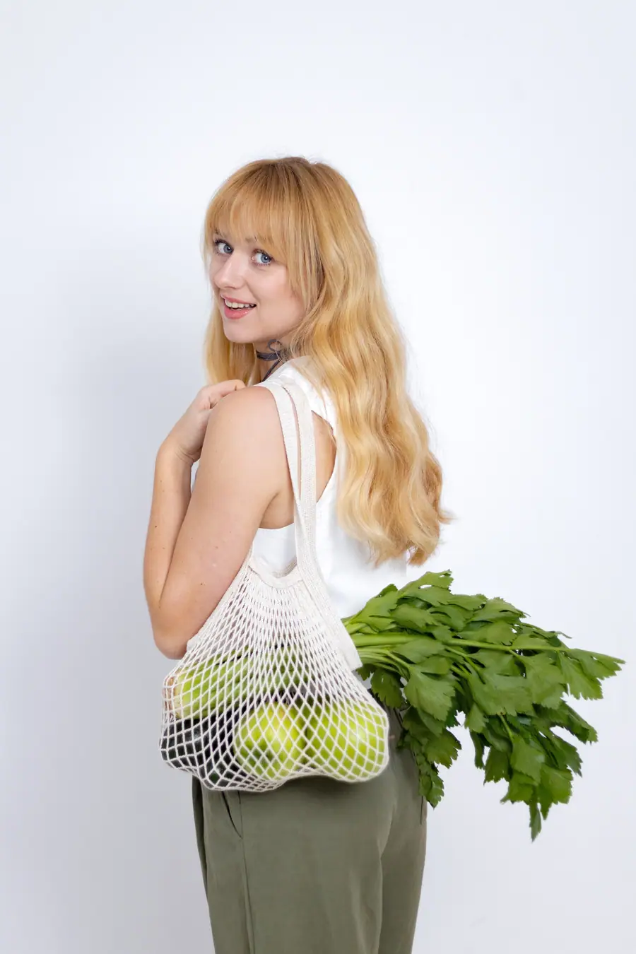 Woman carrying a string bag of apples and fresh herbs